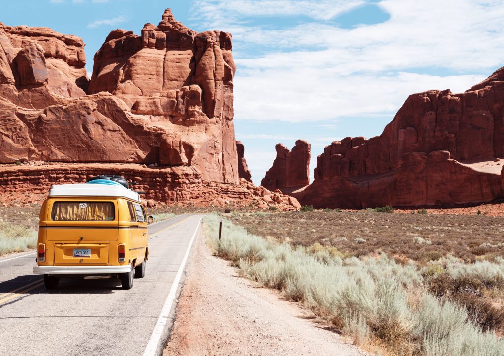 Yellow van driving on desert road surrounded by cliffs